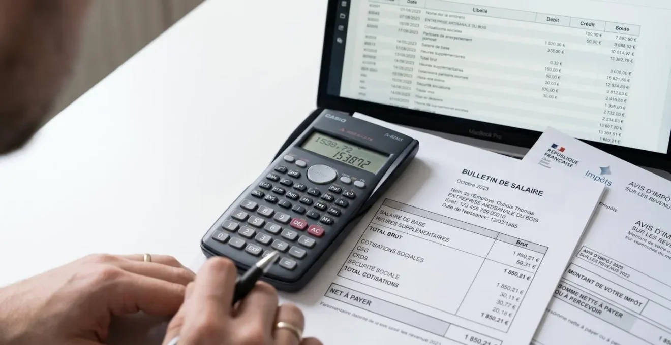 Vue plongeante sur calculatrice professionnelle, écran affichant tableau de ressources et documents administratifs français (fiche de paie et avis d'imposition) sur bureau blanc